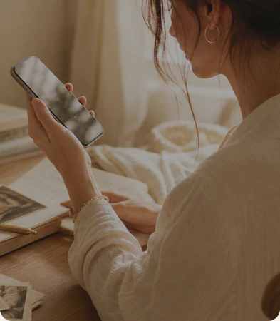 A woman speaks into her phone at a sunlit desk, an open photo album beside her